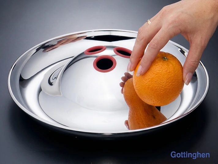 Hand placing an orange into a Gottinghen polished stainless steel bowl with a pierced dome centre
